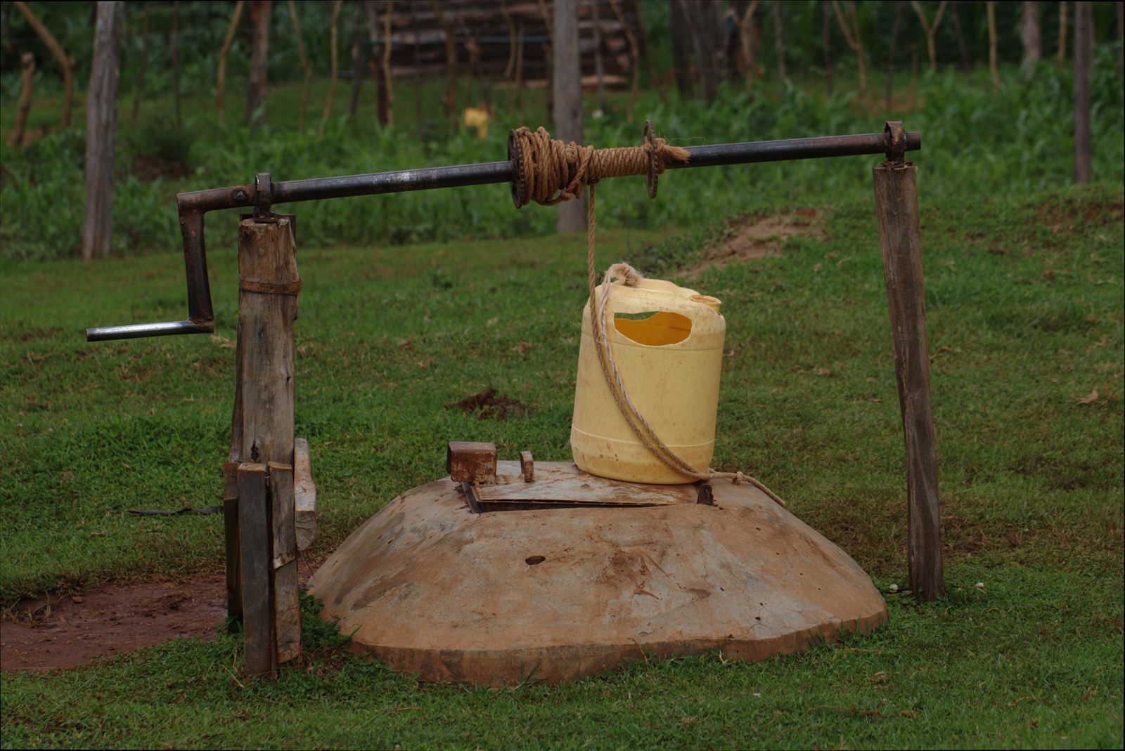 A covered wellhead on a concrete apron, with a rope winch and a water container